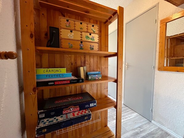 Une étagère en bois contenant divers jeux de société, avec une porte visible au fond.