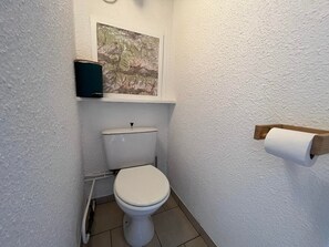 A small, white-walled bathroom with a toilet, a wooden toilet paper holder, and a map on the wall.