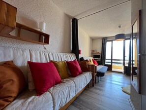 A modern living room with a sofa, a television, and a dining area. - Cozy Mini T2 in Barcelonnette - For 4, sunny balcony (Barcelonnette)