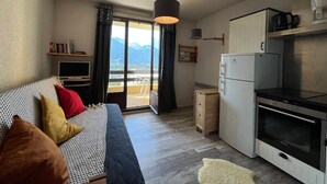 A bedroom with a bed, a TV, and a balcony with a mountain view. - Cozy Mini T2 in Barcelonnette - For 4, sunny balcony (Barcelonnette)