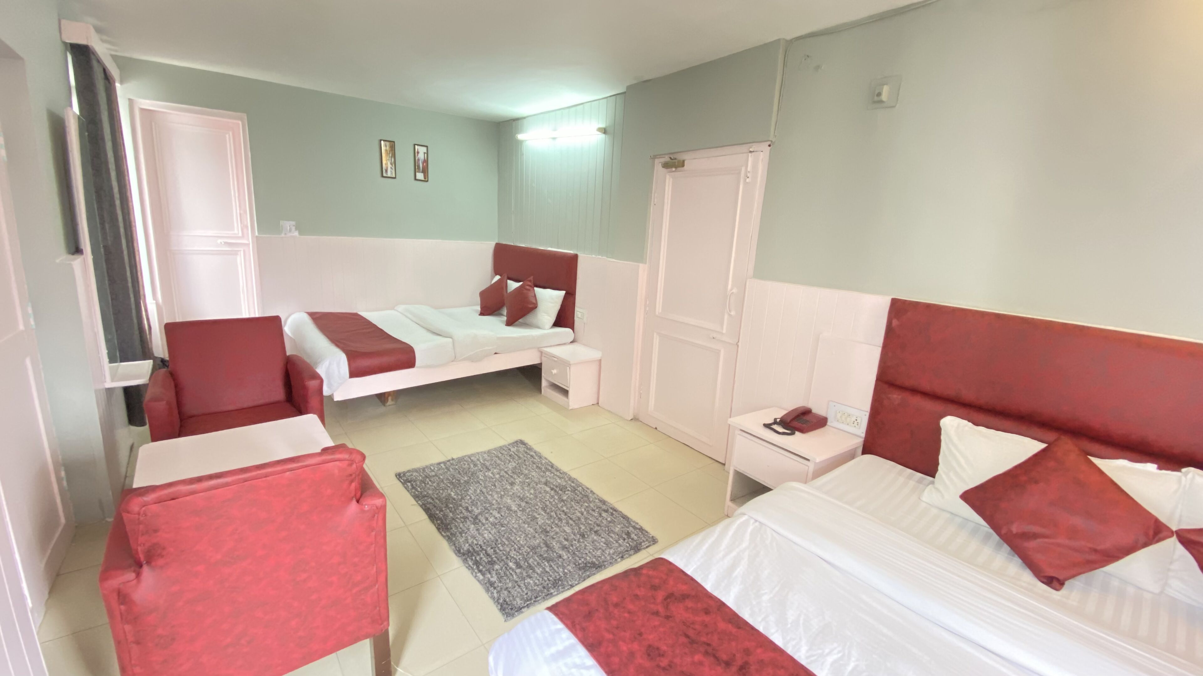 Une chambre avec deux lits, une chaise rouge, une table de chevet avec un téléphone et un petit tapis.