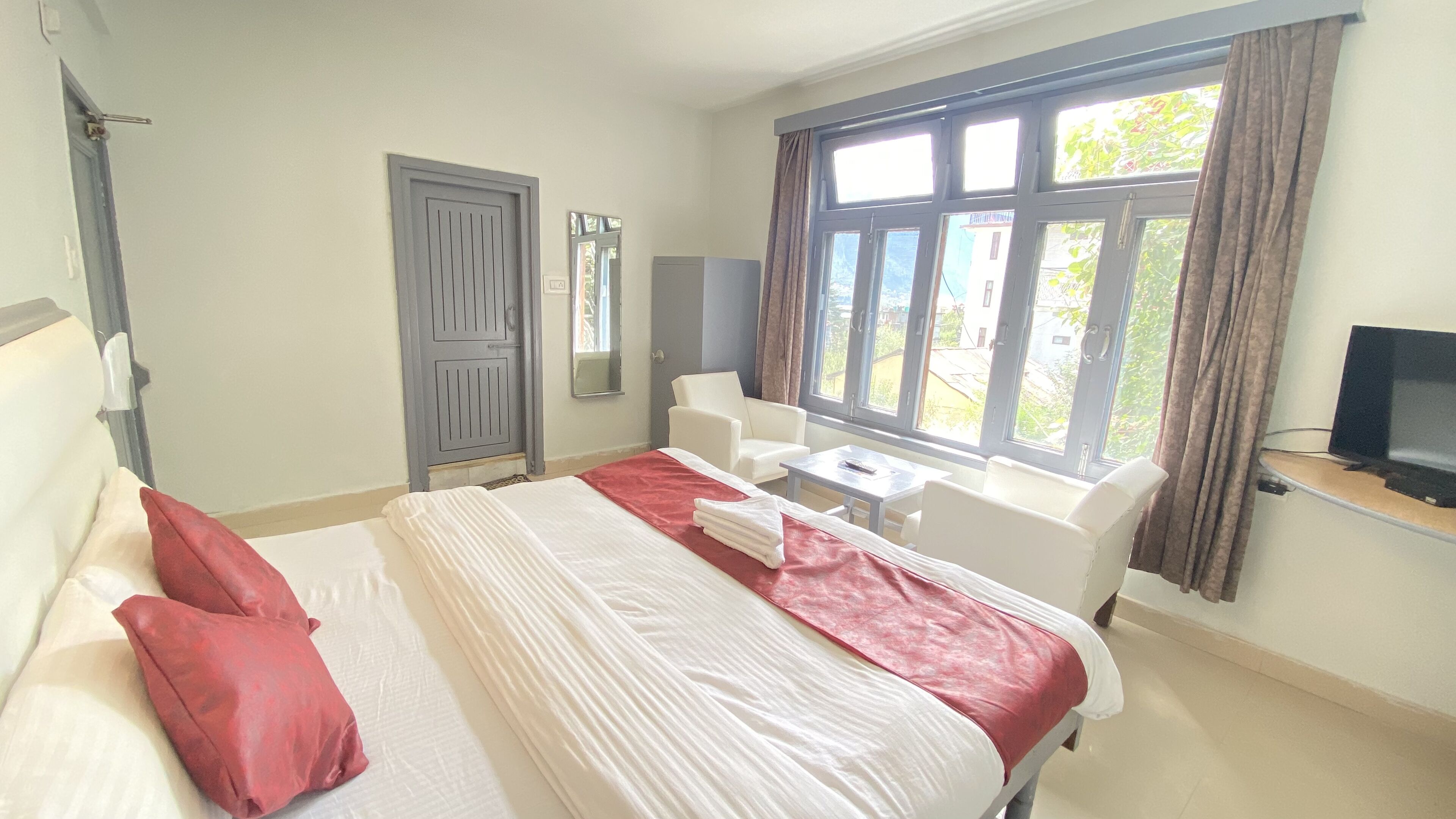 Hotelkamer met een bed, bureau, stoel, televisie en raam met gordijnen.