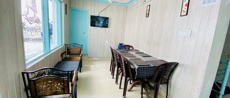 Un comedor con una mesa larga, varias sillas, un televisor montado en la pared y una ventana con vistas al exterior.