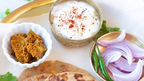 A plate with two pieces of flatbread, a small bowl of chutney, sliced onions, and a bowl of yogurt with red spice. - Hotel Meadows (Manali)