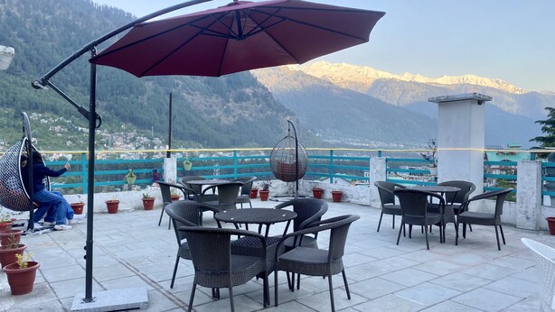 A terrace with wicker furniture, a hanging chair, and a view of snow-capped mountains. - Hotel Meadows (Manali)