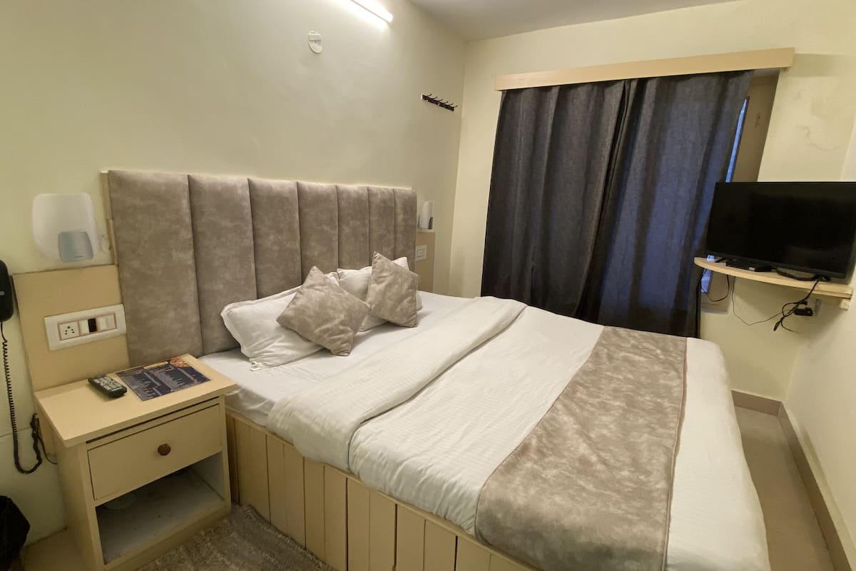Hotellihuone, jossa on sänky, yöpöytä, lamppu, puhelin, televisio ja ikkuna, jossa on verhot.