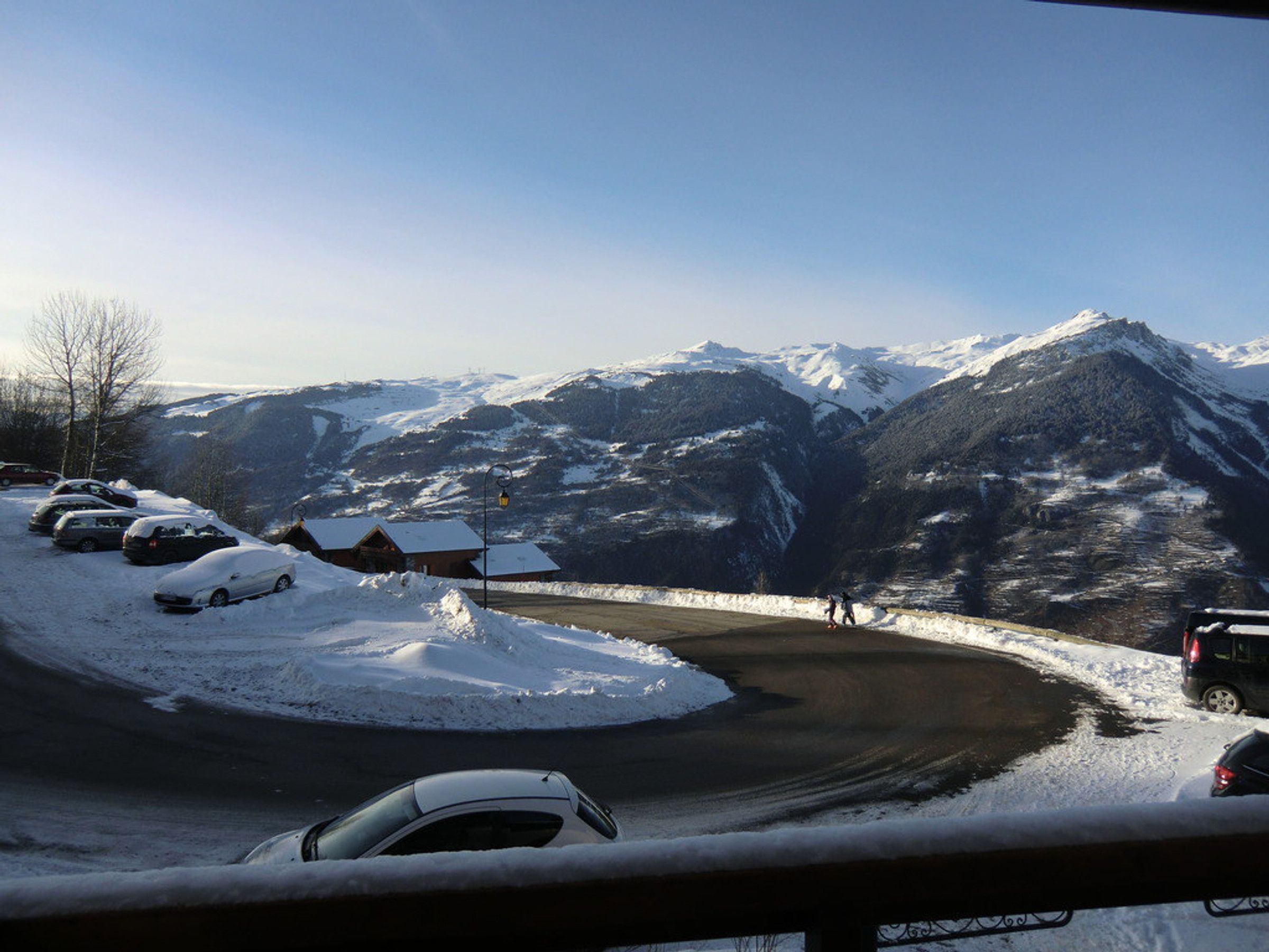 A snow-covered mountain road with parked cars and a building in the foreground.