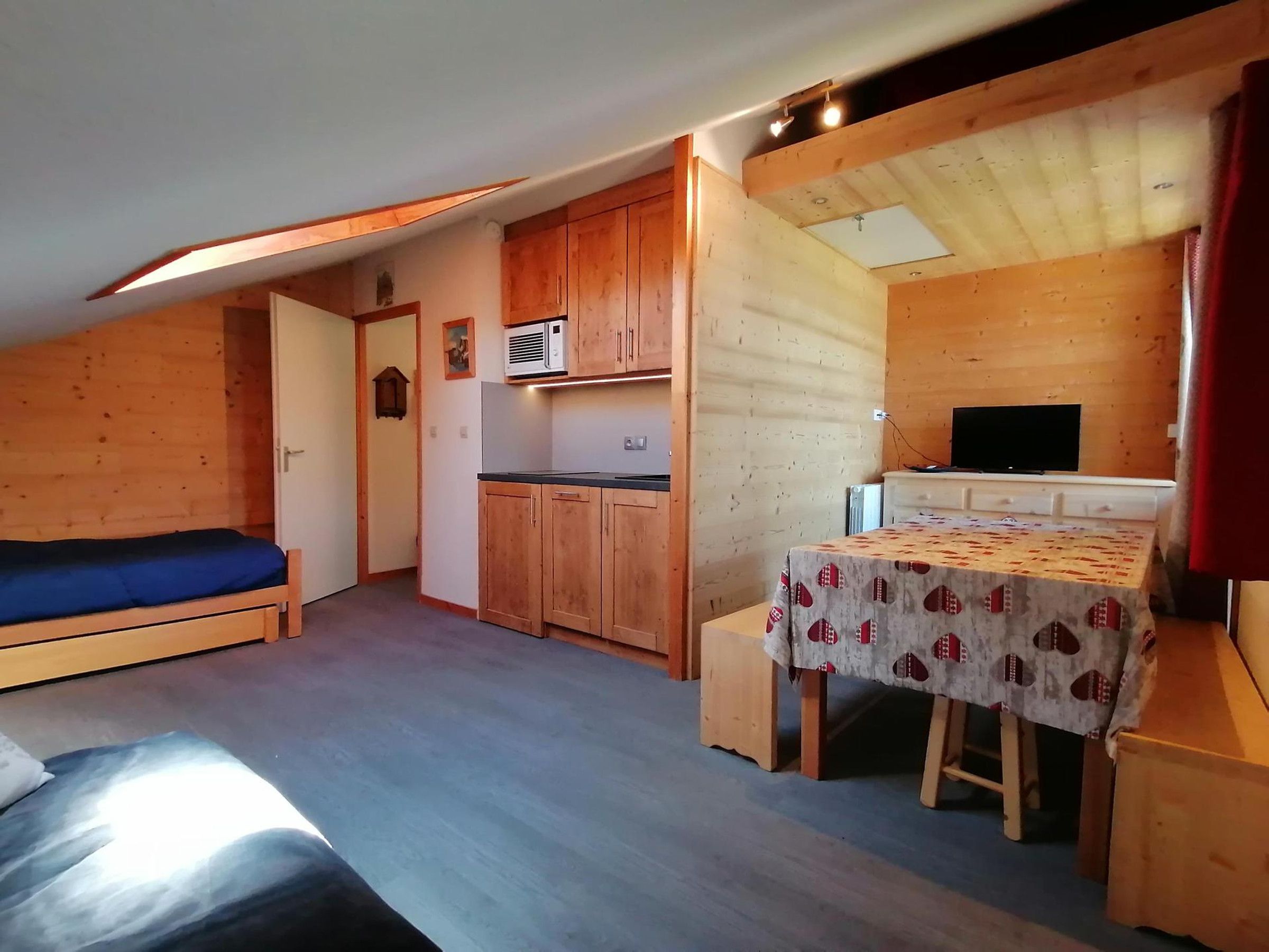 Een kleine kamer met een bed, kitchenette en een eethoekje.
