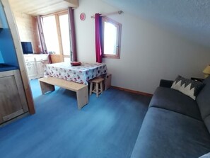 Ein Zimmer mit einer hölzernen Bank, einem Tisch mit gemustertem Tuch, einer Couch und einem Fenster mit Vorhängen.