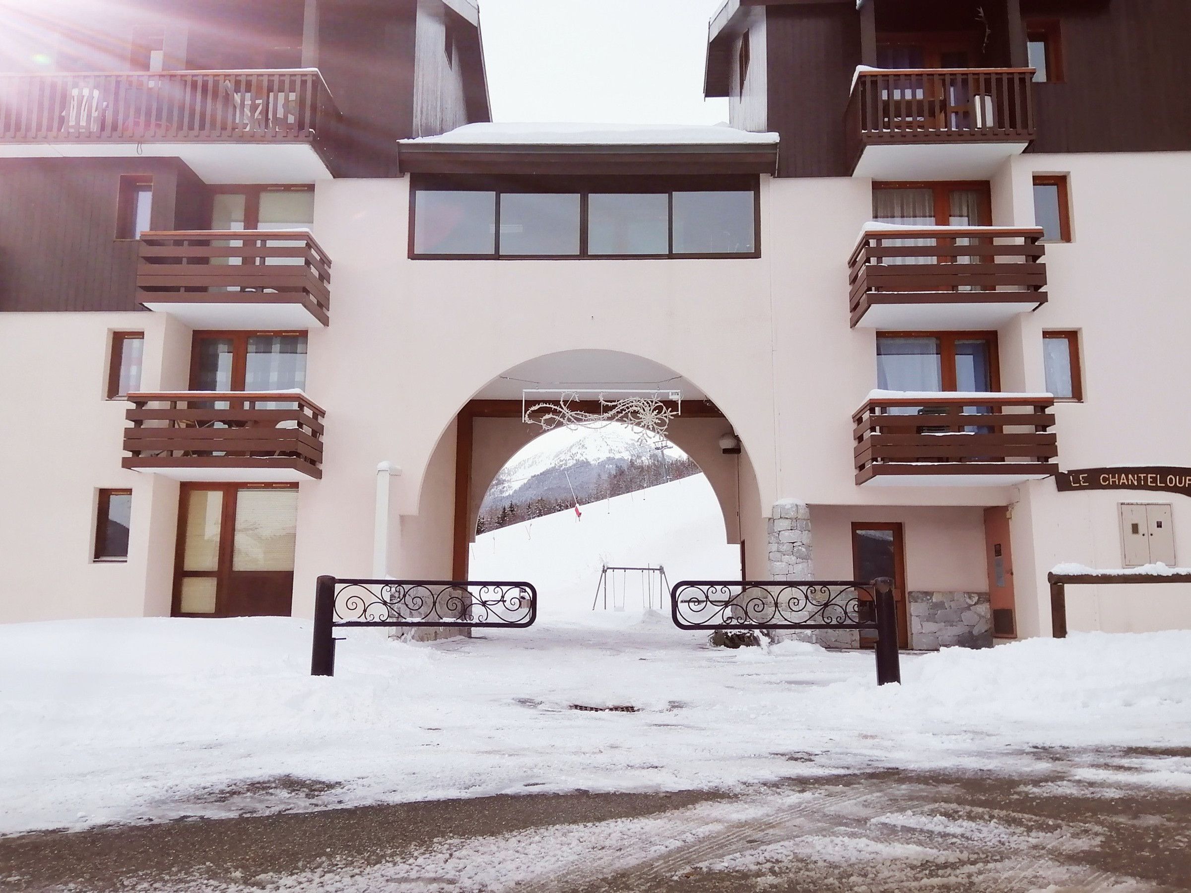 A snow-covered entrance to a building with a balcony and a sign that reads "LE CHANTELOUF".