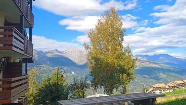 Vista de la montaña con un banco de madera y un edificio con balcones.