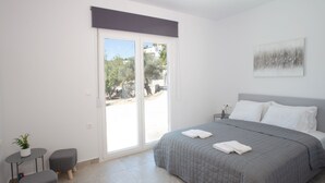 A bedroom with a bed, a nightstand, a potted plant, and a sliding glass door leading to an outdoor area. - 3-bed Villa in Palaioloutra With Private Pool (Agios Vasileios)