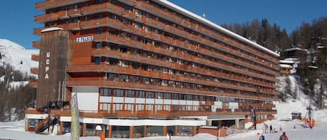 Un hôtel à plusieurs étages doté de balcons, d’un télésiège et surplombant un paysage enneigé.