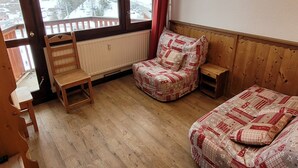 A cozy room with a wooden bench, a cushioned chair, and a bed, featuring a view of a snowy landscape through large windows. - Renovated studio, direct access to slopes, balcony, all comfort (La Plagne)