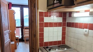 A kitchen with a red and white tiled backsplash, a stainless steel stove, and a wooden door leading to a balcony. - Renovated studio, direct access to slopes, balcony, all comfort (La Plagne)