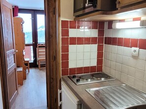A kitchen with a red and white tiled backsplash, a stainless steel stove, and a wooden door leading to a balcony.