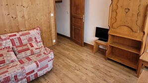 A cozy room with a wooden floor, a patterned sofa, a wooden wardrobe, and a television on a small table. - Renovated studio, direct access to slopes, balcony, all comfort (La Plagne)