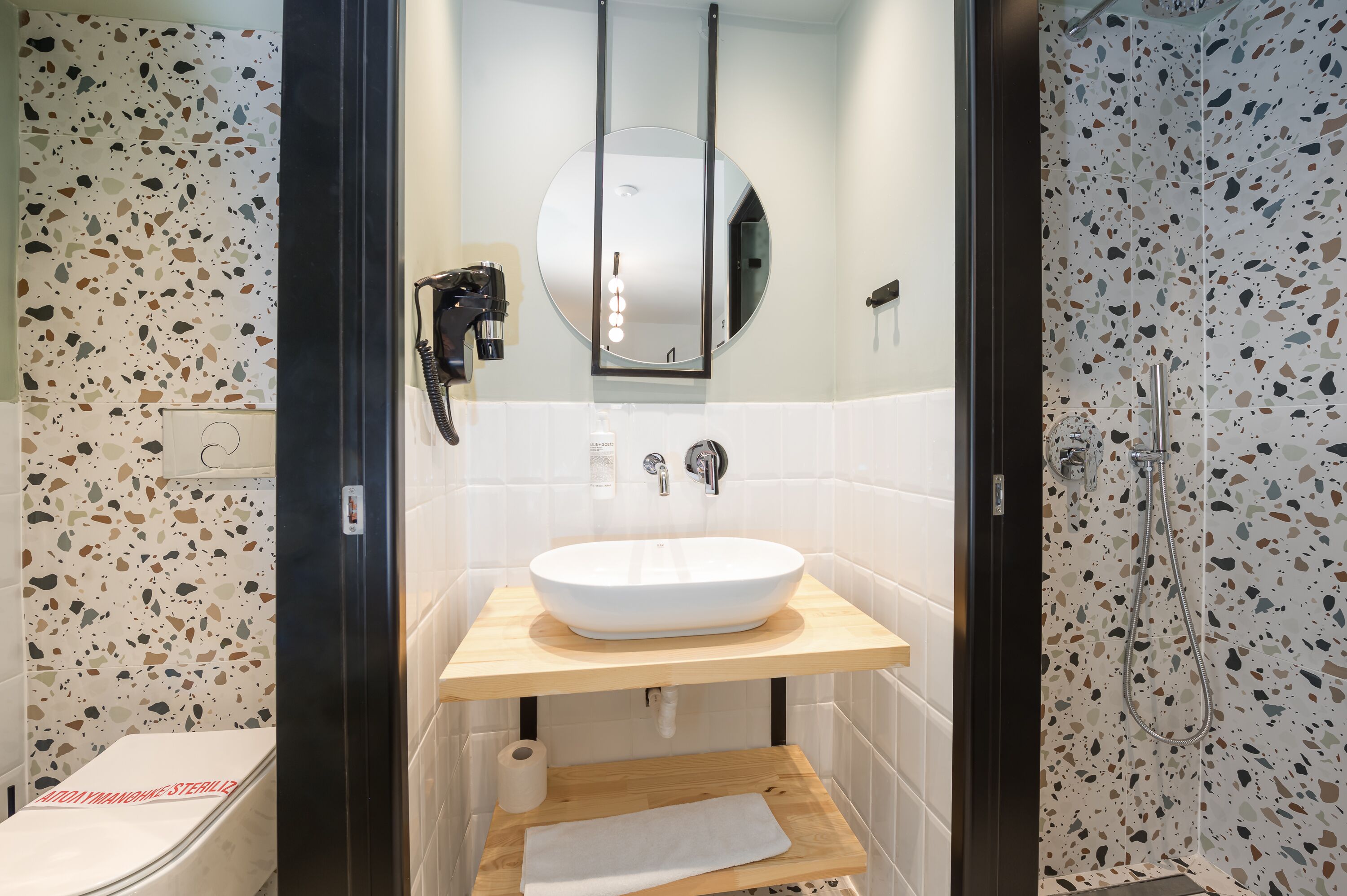 Ein modernes Badezimmer mit einem runden Spiegel, einem weißen Waschbecken und einer Dusche.