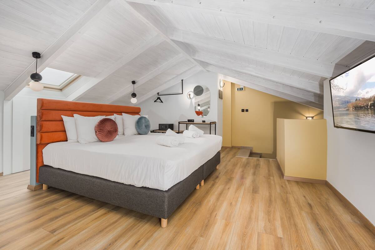 A modern bedroom with a sloped ceiling, a large bed with white bedding, and a skylight.