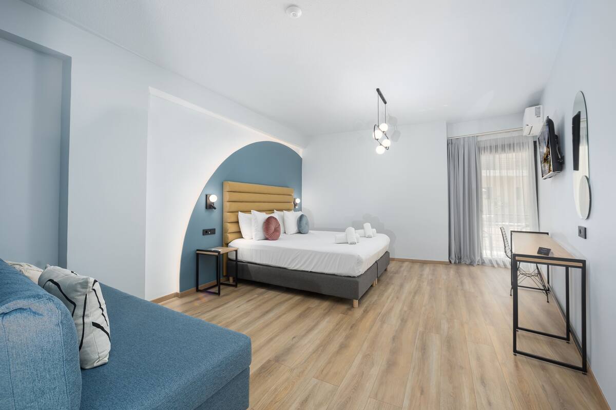 A modern hotel room with a bed, a desk, and a blue sofa.