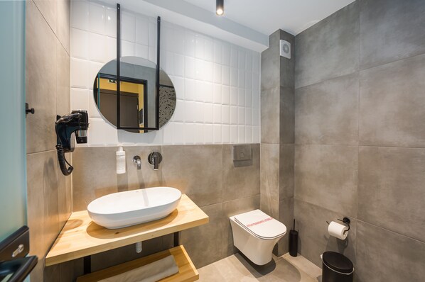 A modern bathroom with a round mirror, a white sink, a toilet, and a trash bin. - Centro Urban Stay (Ioannina)