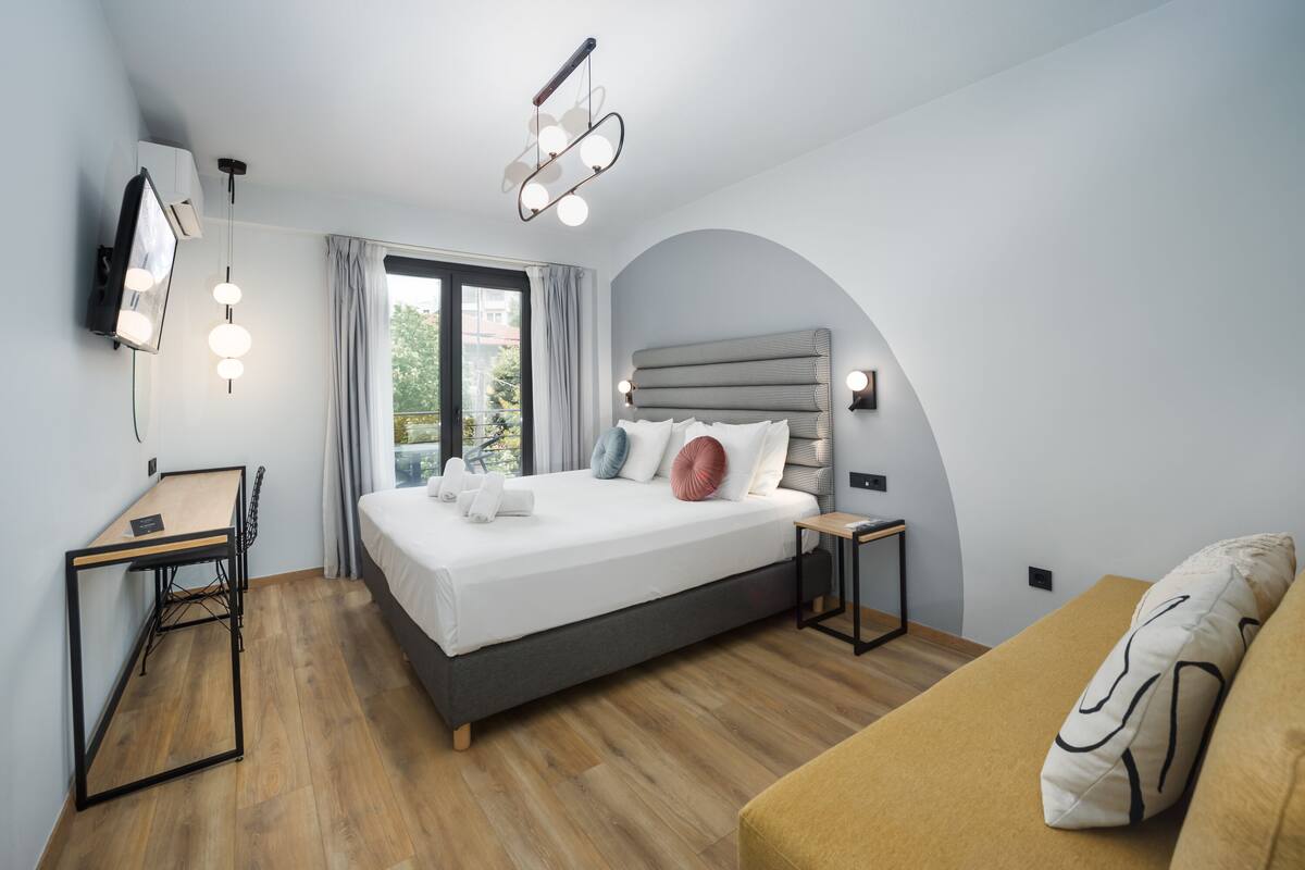 A modern bedroom with a bed, bedside tables, a desk, and a sofa.
