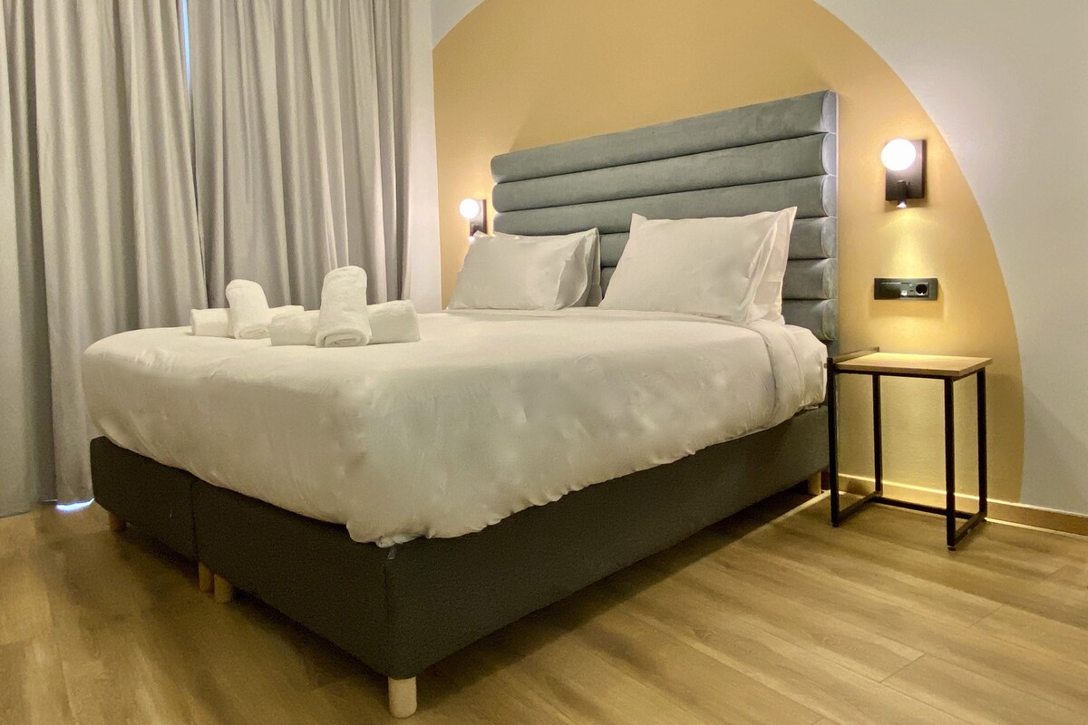 Une chambre d’hôtel moderne avec un grand lit, une table de chevet et un luminaire fixé au mur.