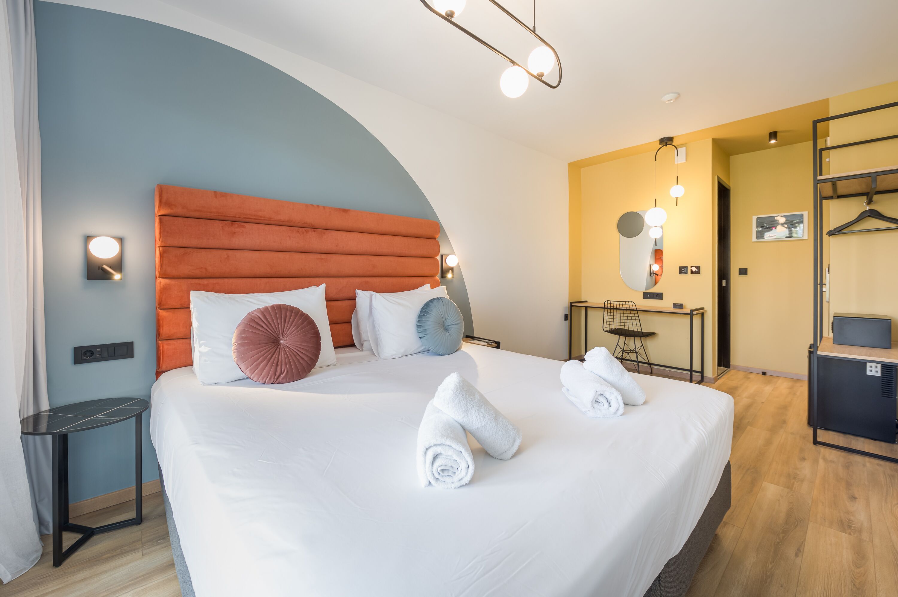 Habitación de hotel con una cama grande, una mesita de noche, un escritorio con una silla, un espejo y un armario.