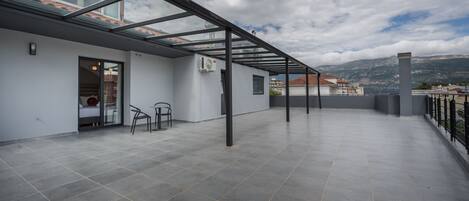 A spacious rooftop terrace with a glass ceiling, a seating area, and a view of the cityscape and mountains.