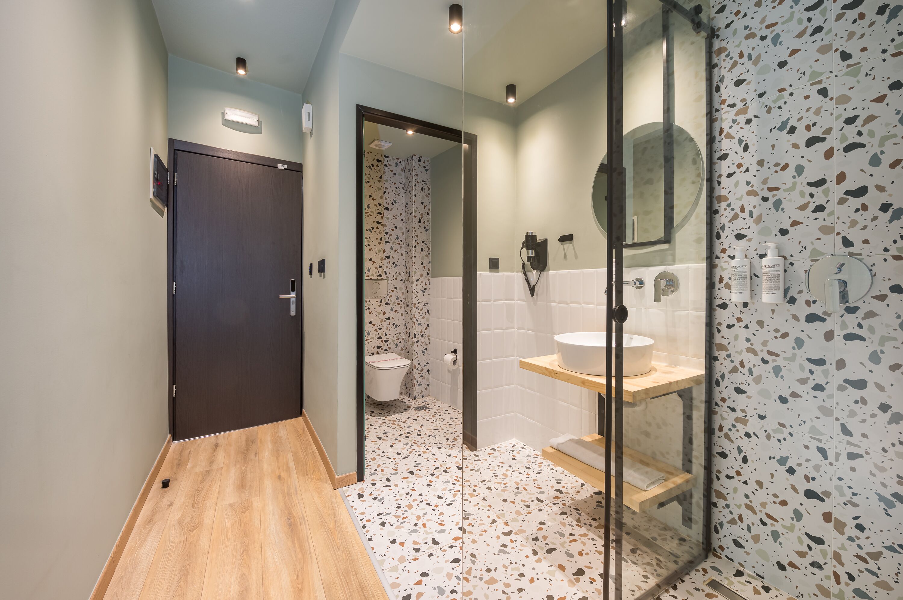 Un baño moderno con suelo de madera, cabina de ducha de vidrio y lavabo blanco con encimera de madera.