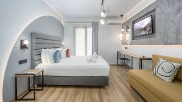 A modern hotel room with a bed, a sofa, a desk, and a TV mounted on the wall.