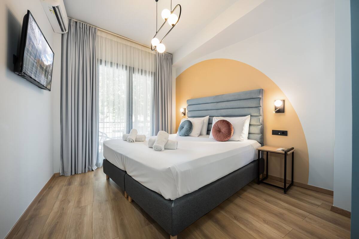 A modern bedroom with a large bed, a TV mounted on the wall, and a bedside table with a lamp.