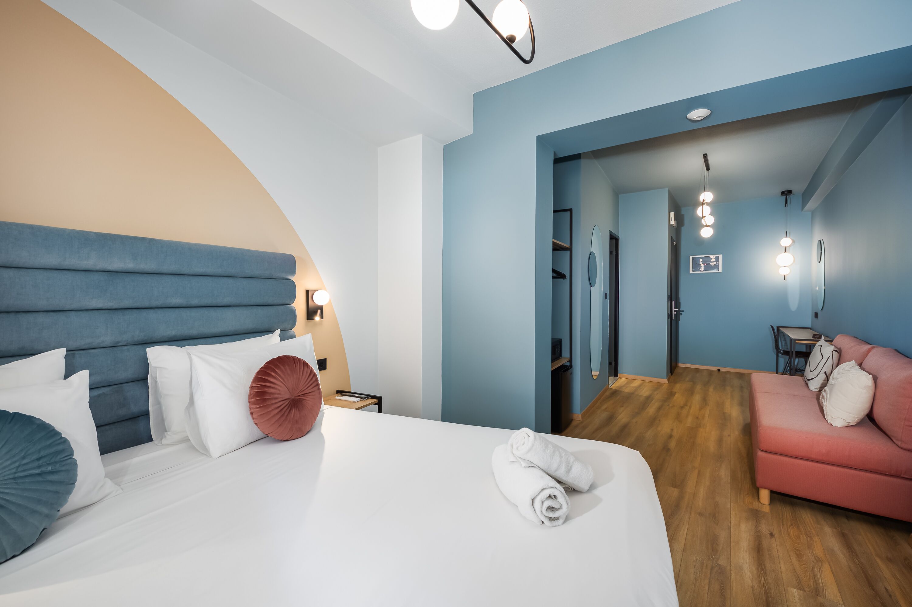 A modern hotel room with a large bed, a pink sofa, and a wooden floor.