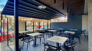 Un café en plein air avec des tables et des chaises, un plafond en bois et une vue sur les voitures garées et les bâtiments.