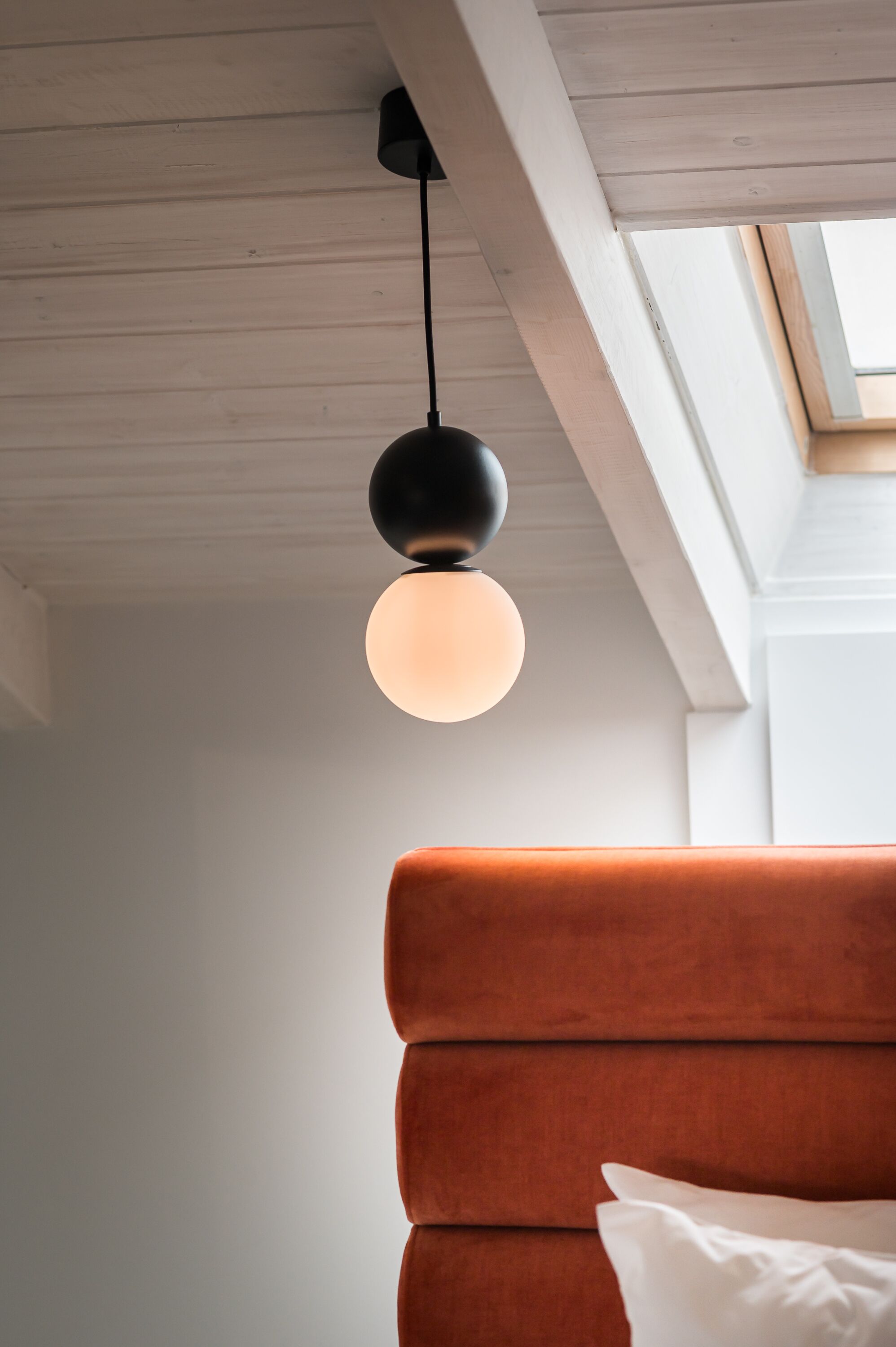 Una habitació moderna amb sostre de fusta, una làmpada penjant rodona i una finestra gran.