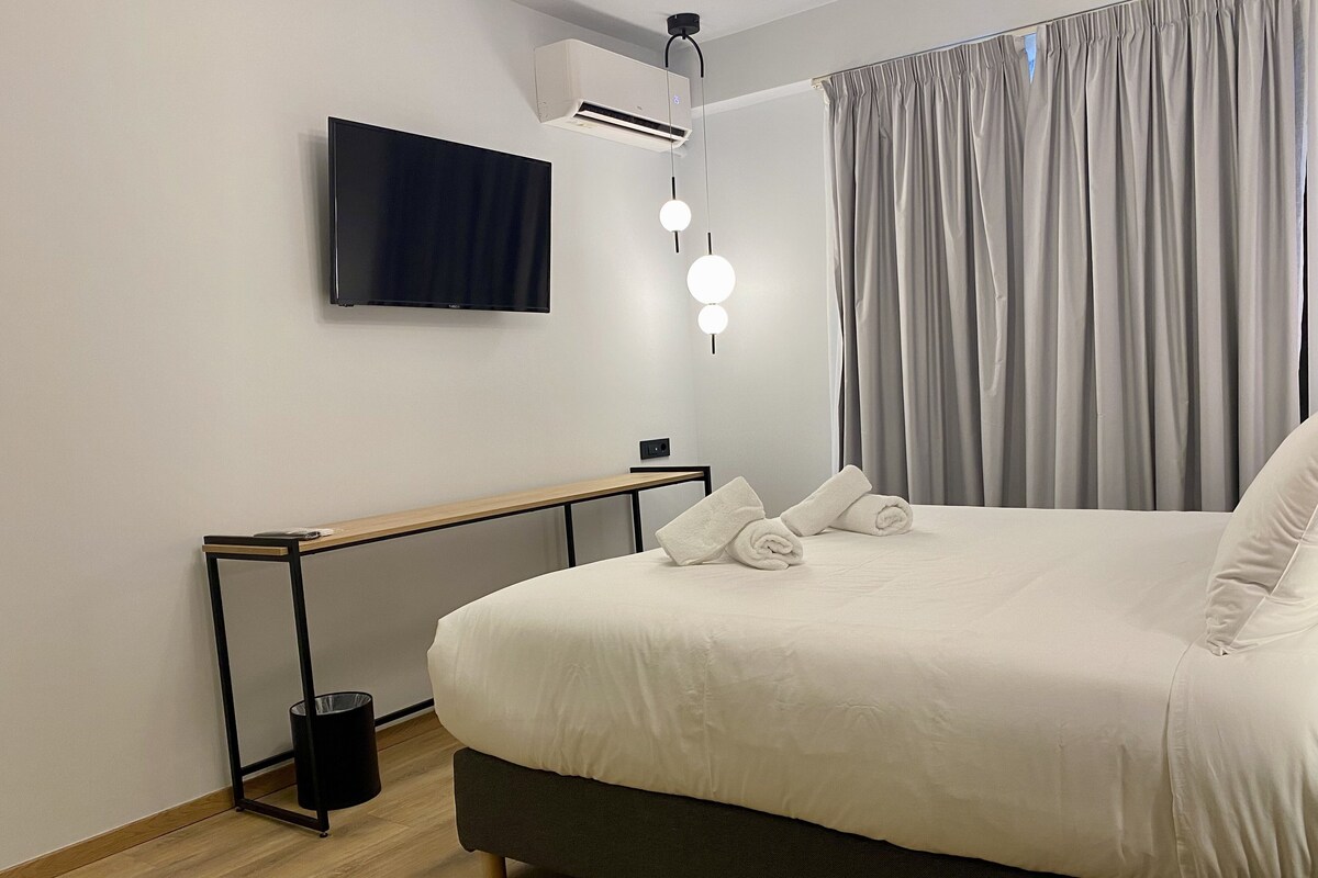 Une chambre d’hôtel moderne équipée d’un lit, d’un téléviseur à écran plat, d’un système de climatisation, d’une table de chevet et d’un rideau.