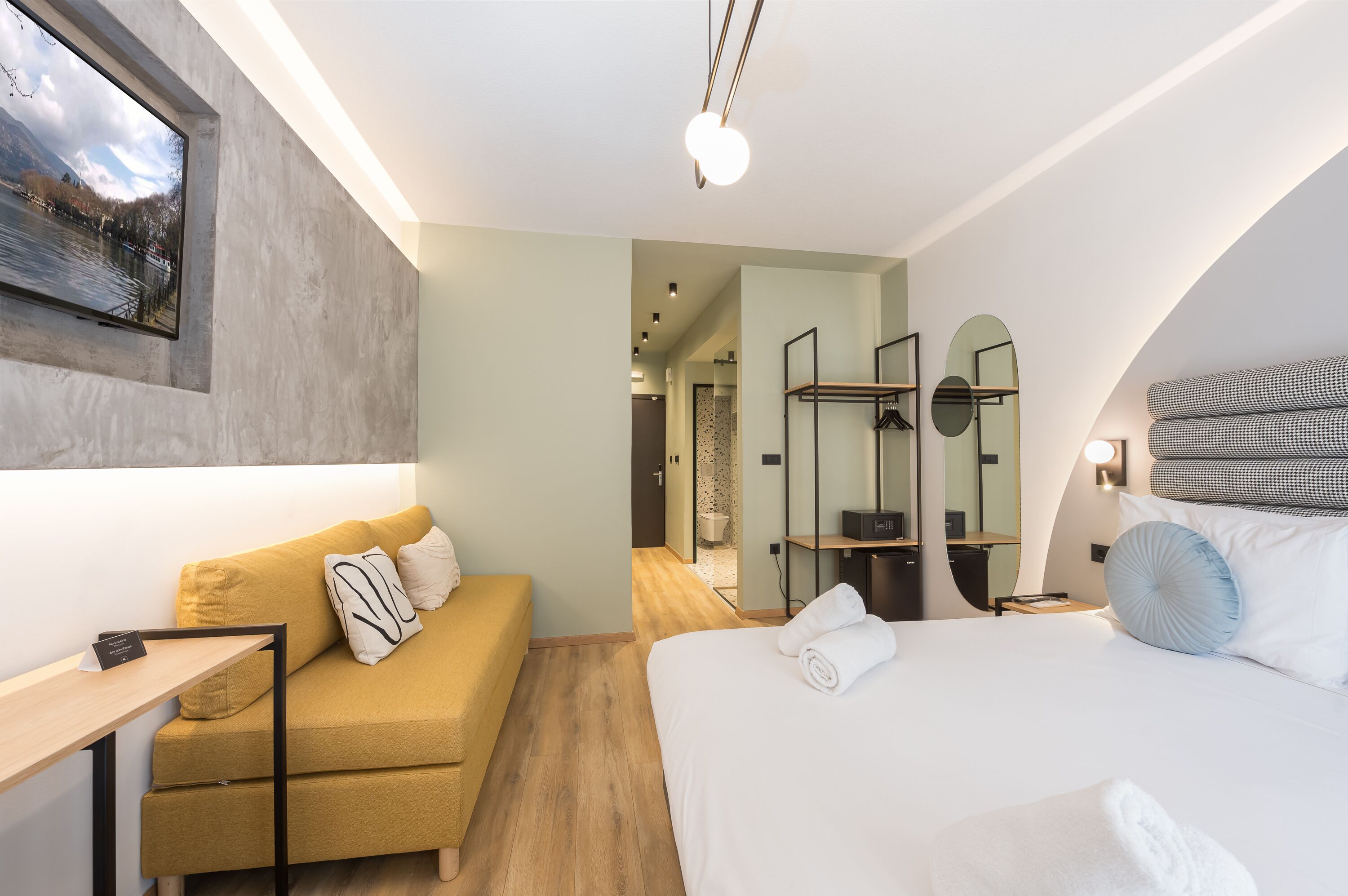 Ett modernt hotellrum med en säng, en soffa, ett litet bord och en spegel.