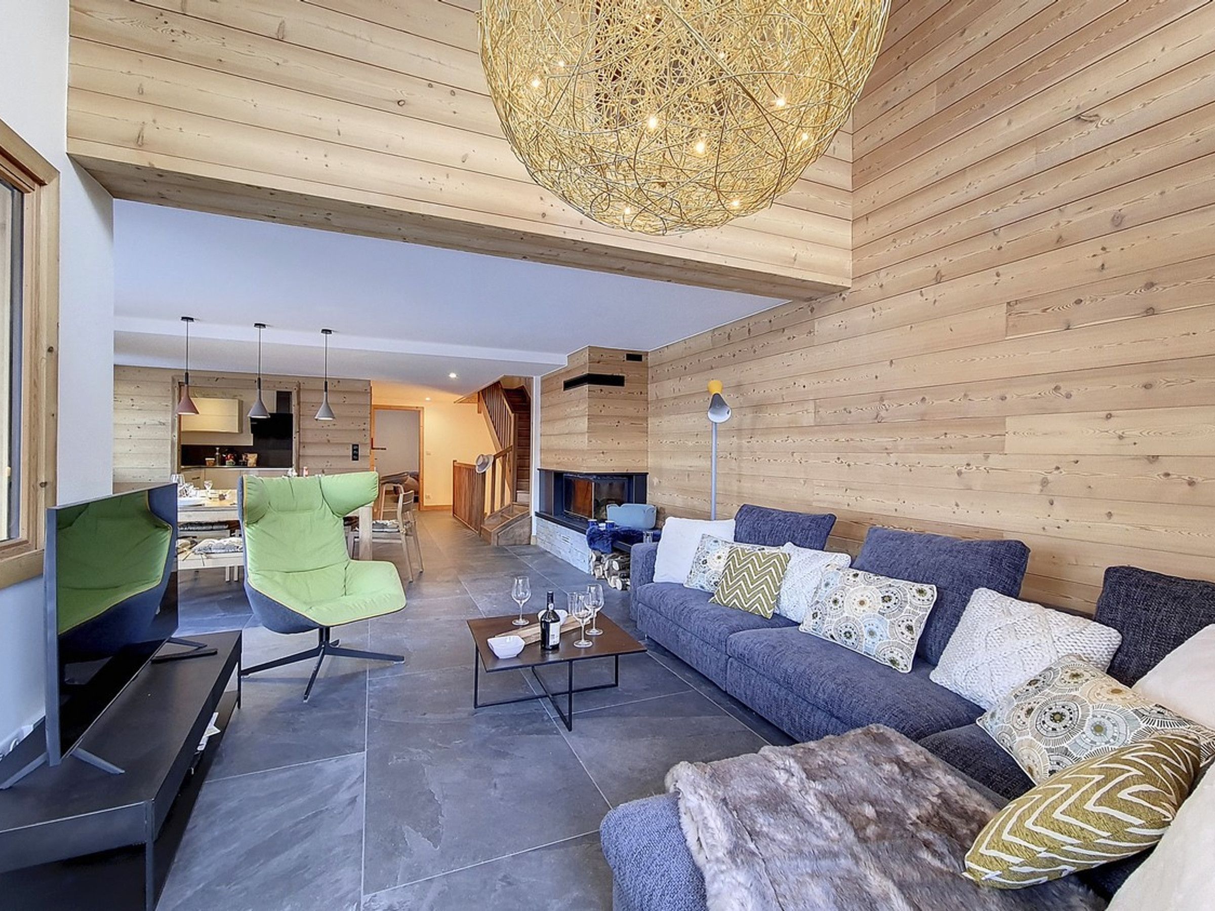 Una sala de estar moderna con chimenea, una butaca verde, un sofá gris y una mesa de centro.