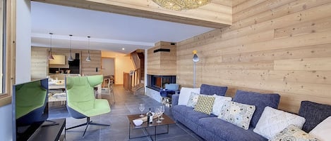 Una sala de estar moderna con chimenea, una butaca verde, un sofá gris y una mesa de centro.
