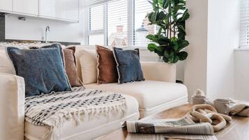 A modern living room with a white sofa, a knitted throw, and a newspaper on a wooden table.
