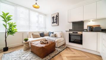 A modern living room with a sofa, ottoman, and a potted plant.