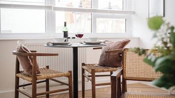 A dining area with a round table, two wicker chairs, a small rug, and a view through large windows.