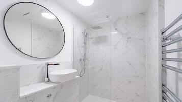 A modern bathroom with a white marble shower, a round mirror, and a white sink.
