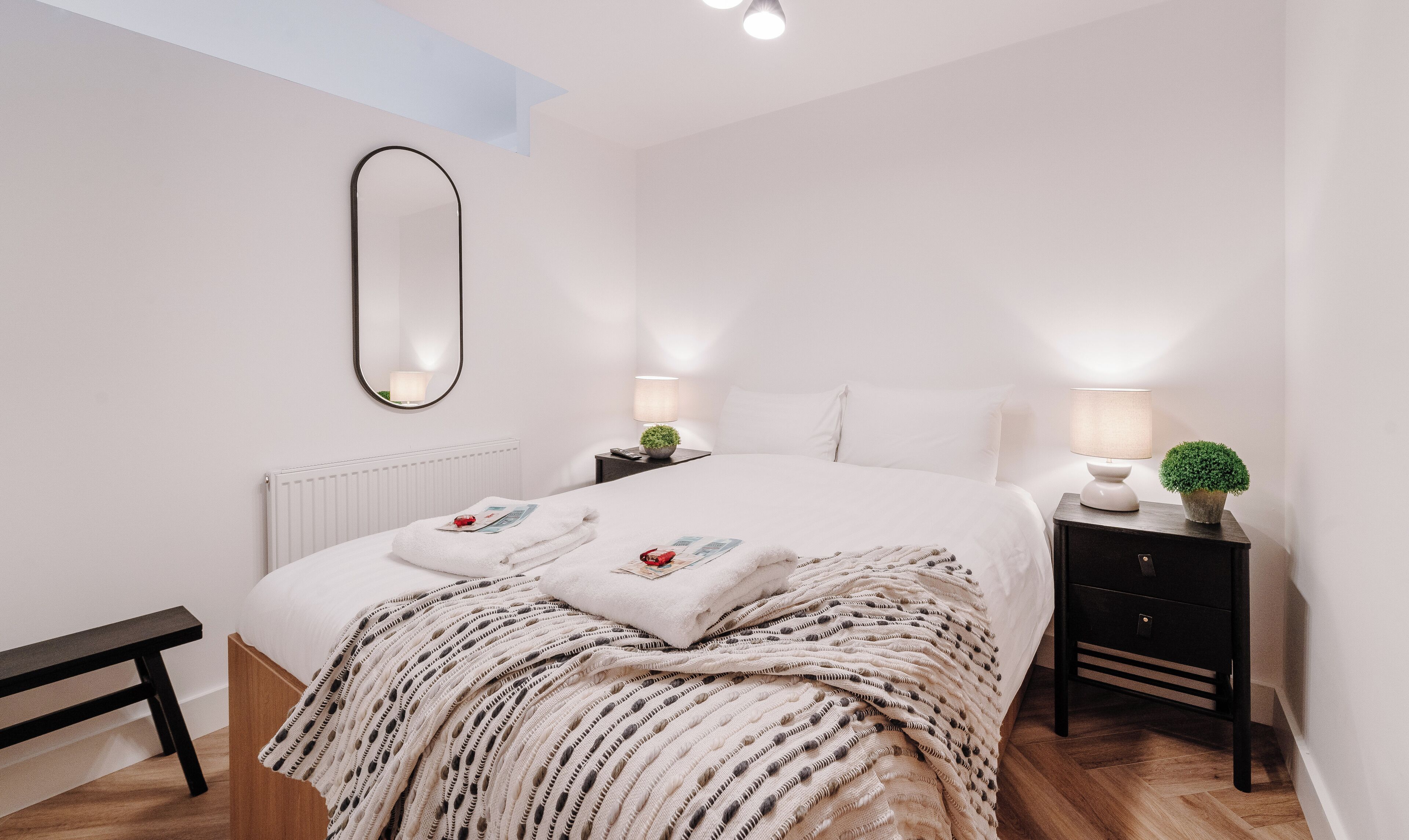 Un dormitorio moderno con una cama grande, mesitas de noche con lámparas, un espejo y un banco.