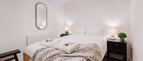Un dormitorio moderno con una cama grande, mesitas de noche con lámparas, un espejo y un banco.