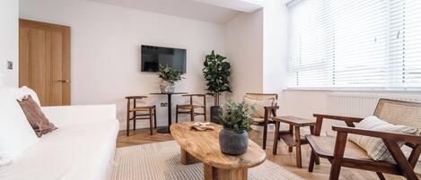 A modern living room with a wooden coffee table, white sofa, and a dining area with chairs and a small table.
