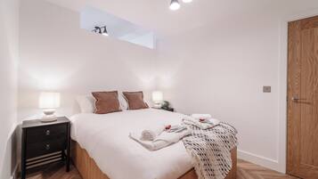 Ein Schlafzimmer mit einem Bett, Nachttischen, einer Stehlampe, einem kleinen Tisch mit Lampe, einer Holztür und einem Oberlicht.