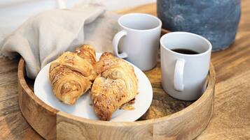 A wooden tray with croissants, two white coffee cups, and a vase with green plants.