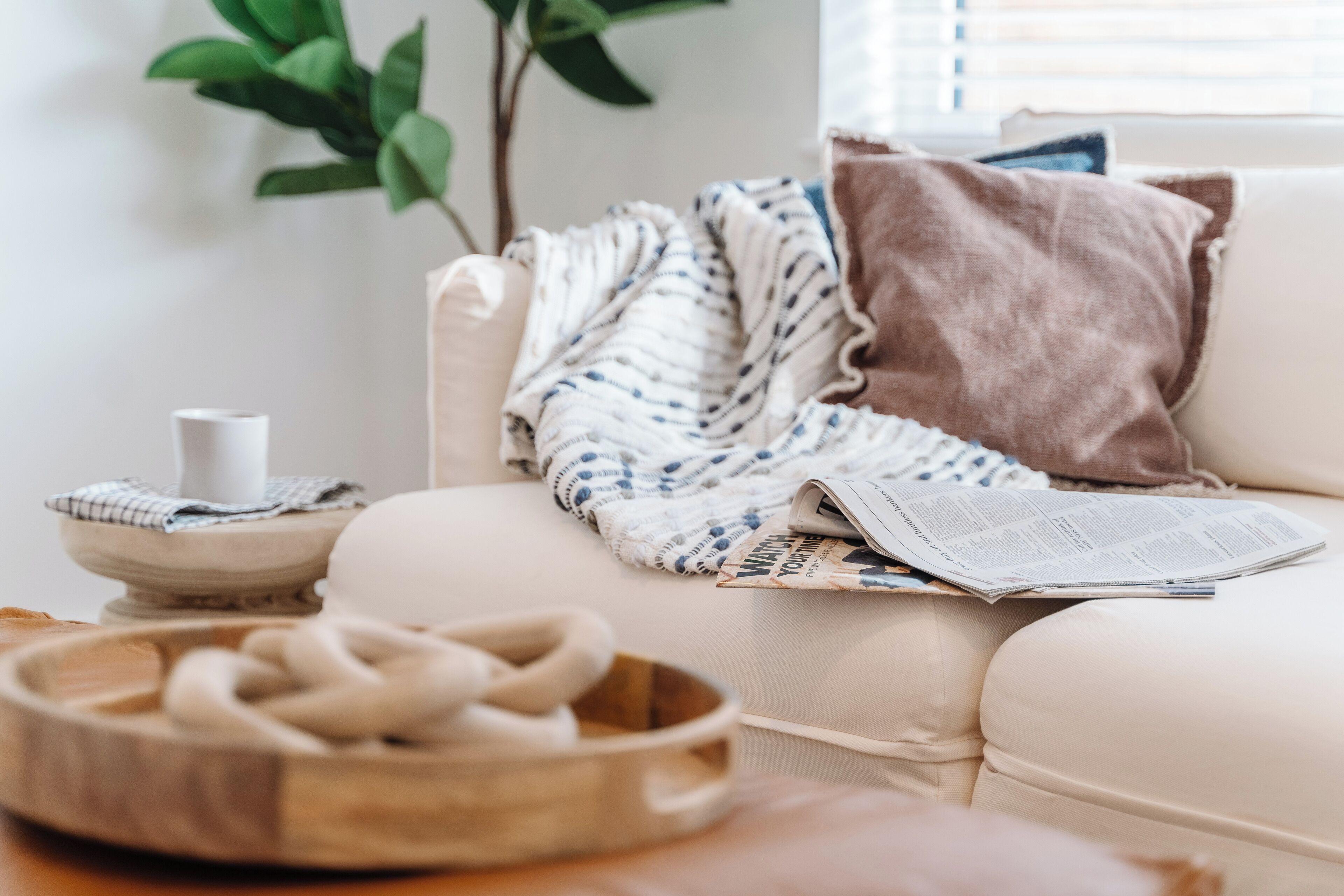 A cozy living room with a beige sofa, a wooden bowl, a white vase, and a plant.