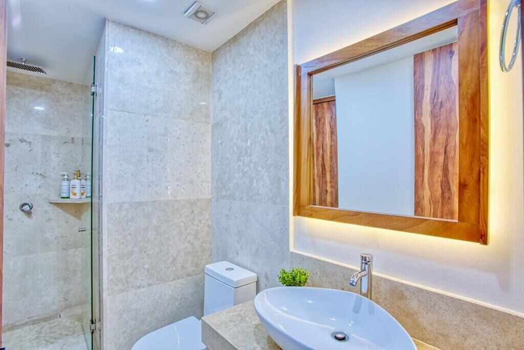 A modern bathroom with a glass-enclosed shower, a white sink, and a wooden-framed mirror.